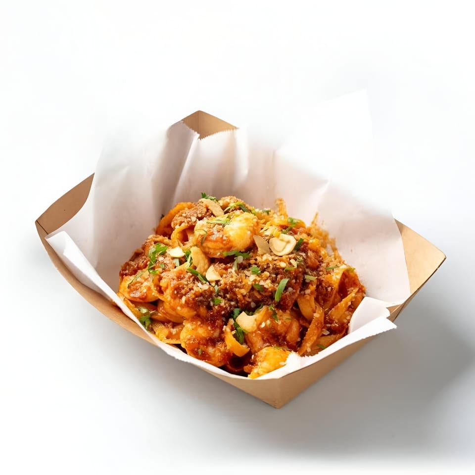 Boil Daddy's shrimp and pasta dish in a brown paper container, garnished with herbs and nuts.